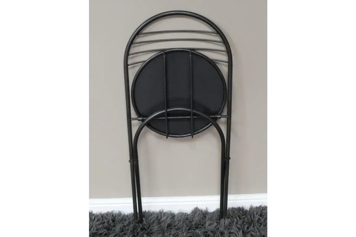 Black metal folding chair with round seat leaning against beige wall on grey rug