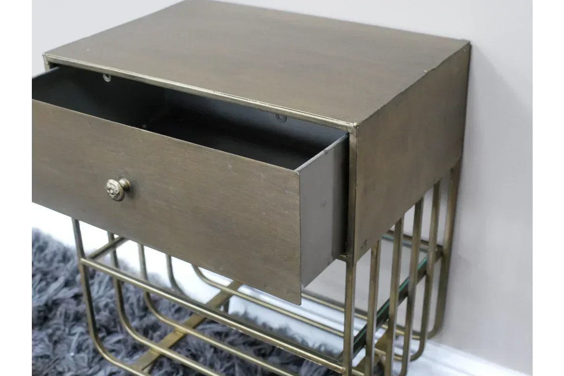 Metal side table with open drawer and brass legs beside a grey rug