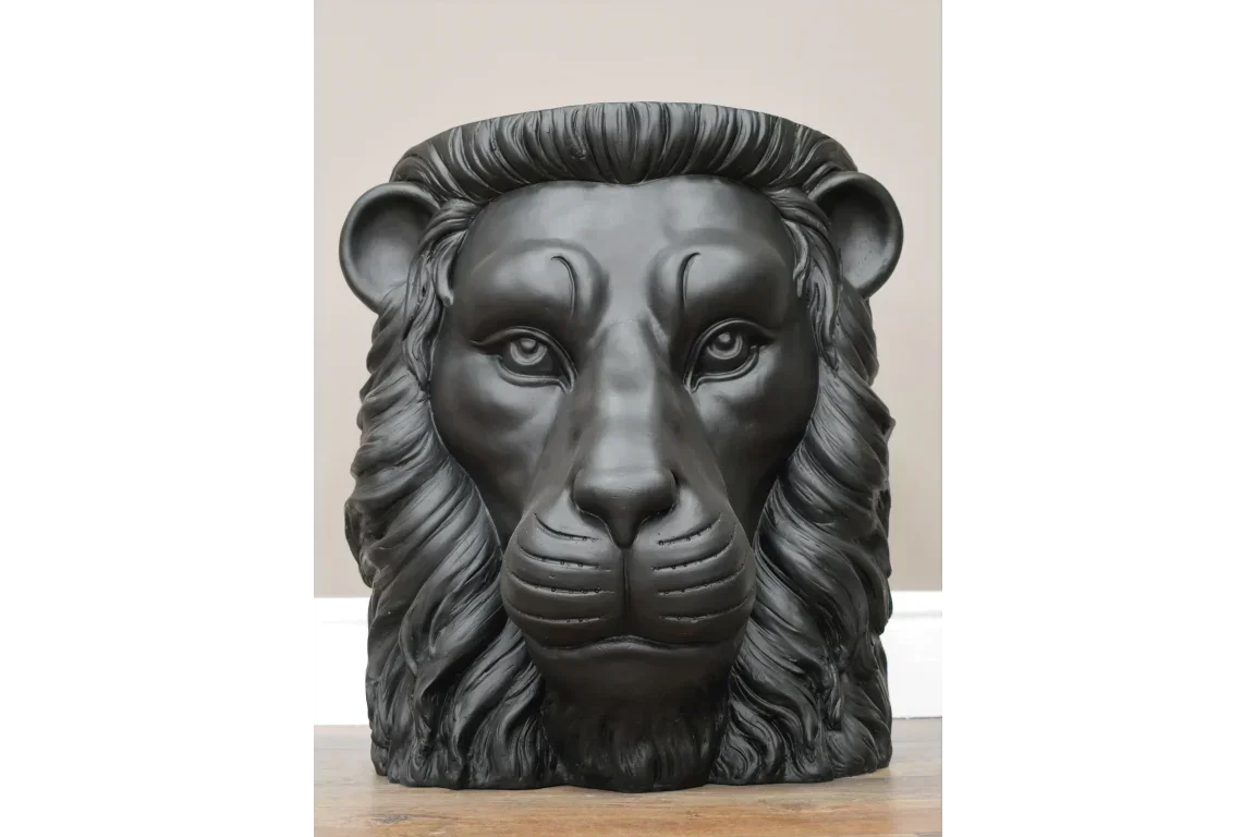 Black lion head planter with detailed mane on wooden floor against neutral wall