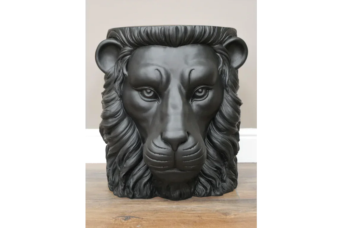 Black lion head planter with detailed mane on wooden floor against neutral wall