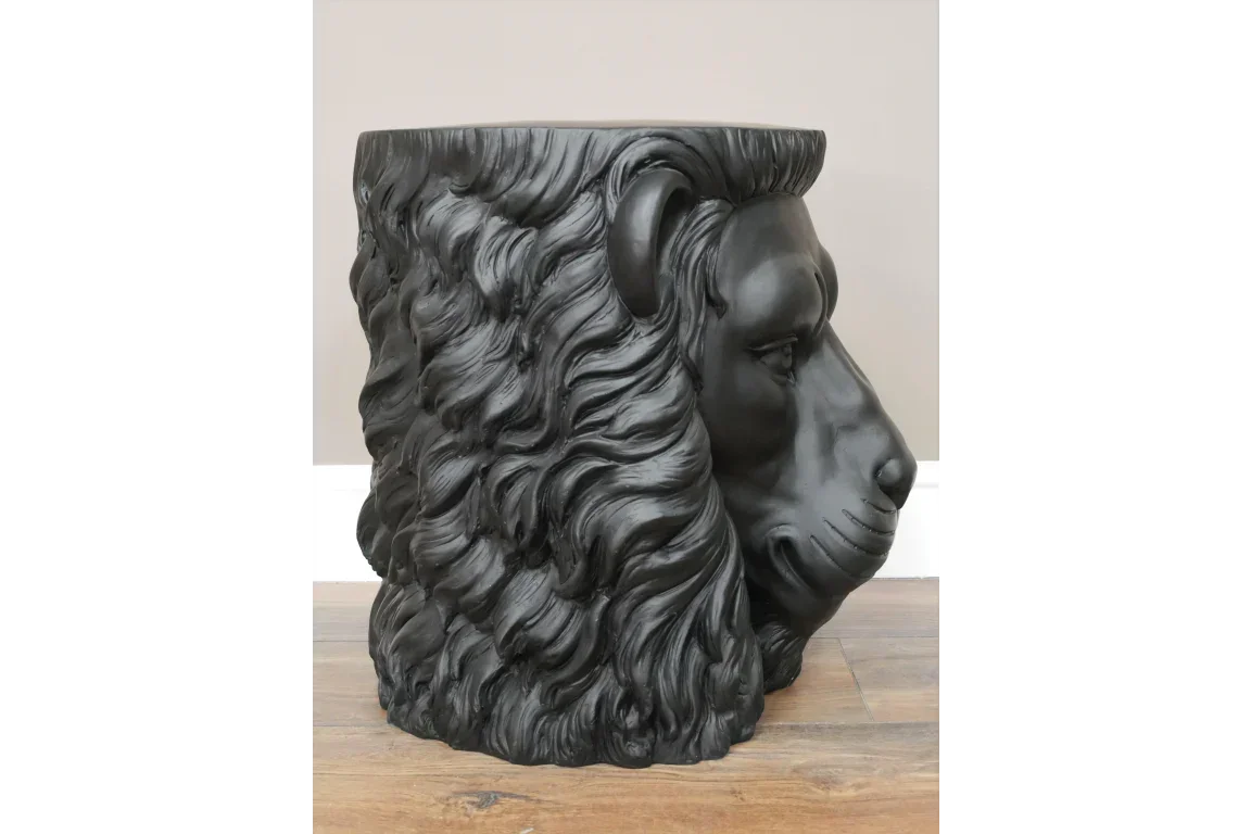 Black lion head side table with detailed mane on wooden floor against beige wall