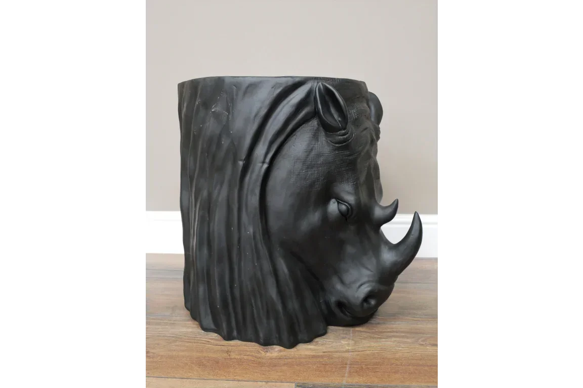 Black rhino head side table with textured surface on wooden floor against light wall