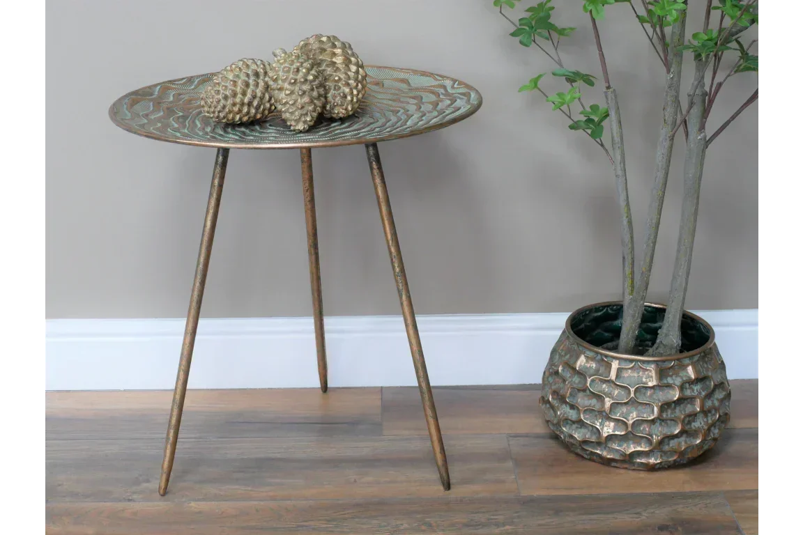 Bronze metal side table with textured top beside decorative plant pot on wooden floor