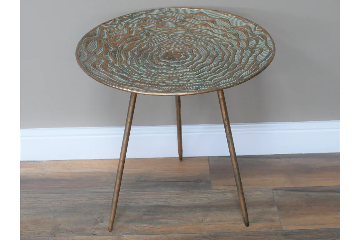 Round metal side table with textured top and three slim legs on wood floor