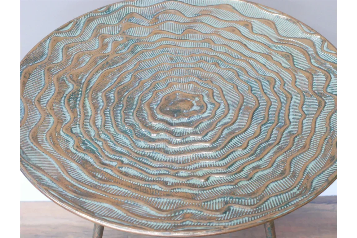 Round metal side table top with textured concentric wave pattern in bronze and teal finish