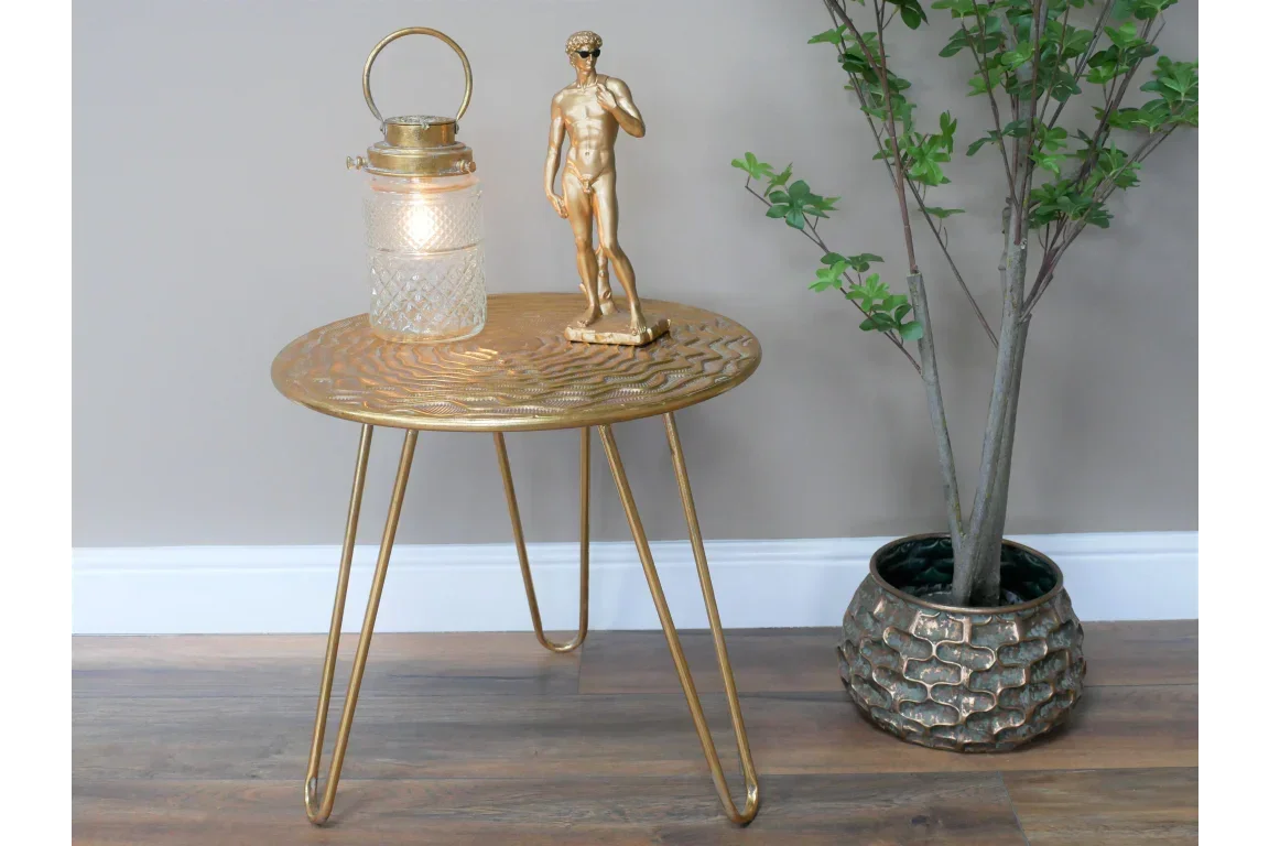 Gold metal side table with hairpin legs, glass lantern, and plant in textured pot