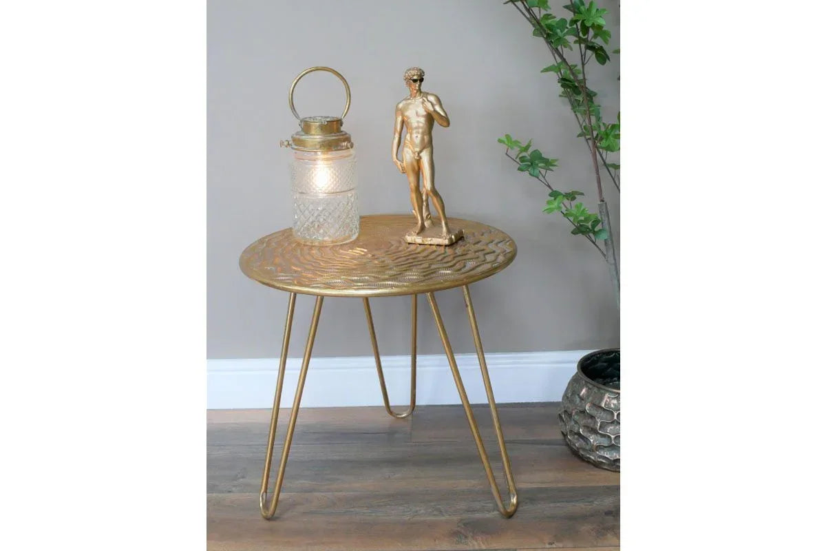 Gold metal side table with hairpin legs, topped with lantern and sculpture, on wooden floor