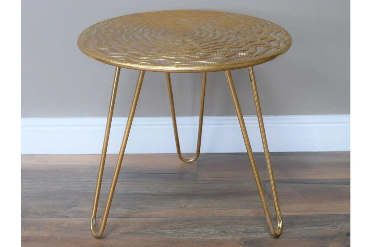 Gold metal side table with textured round top and hairpin legs on wooden floor