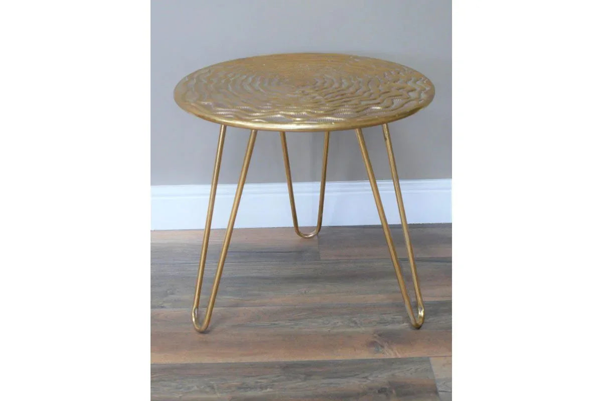 Gold metal side table with textured round top and hairpin legs on wooden floor