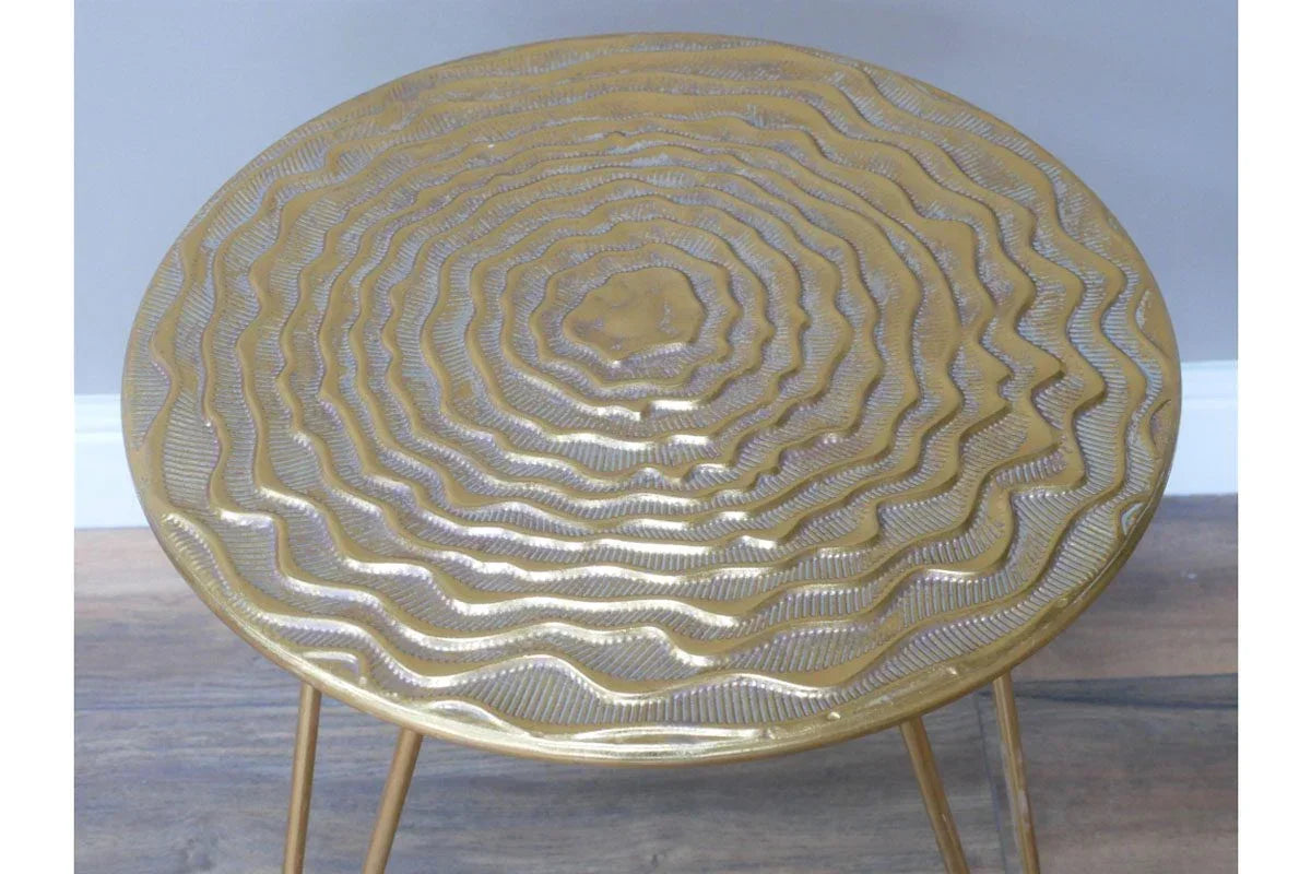 Gold metal side table with textured circular top and slim legs on wooden floor