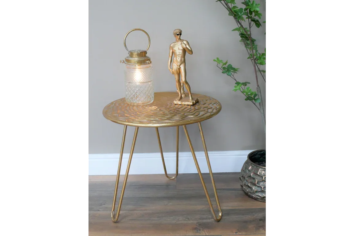 Gold metal side table with hairpin legs, lantern and statue on wood floor beside plant