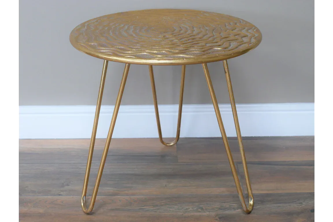Gold metal side table with textured round top and hairpin legs on wooden floor