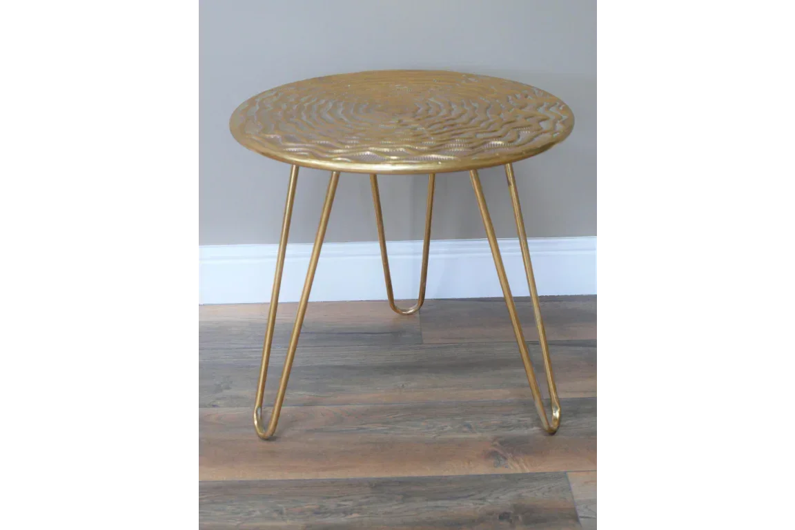 Gold metal side table with textured round top and hairpin legs on wooden floor