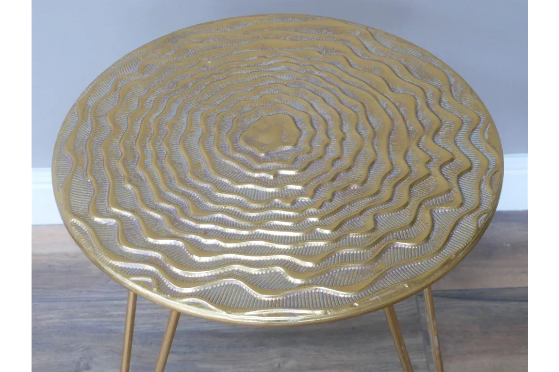 Gold metal side table with textured circular top and hairpin legs on wood floor
