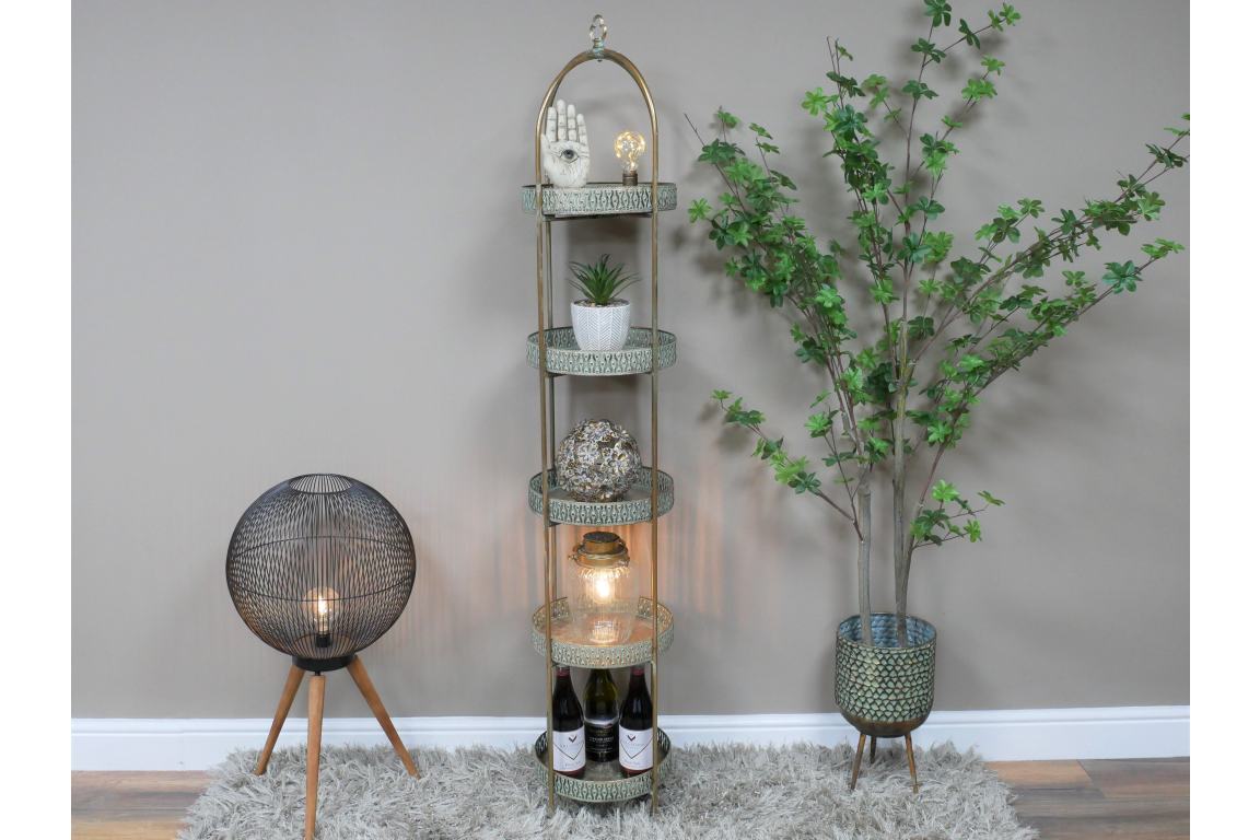 Tall Moroccan style 5 tier metal shelves with intricate pattern, set between a round black lamp and a potted green plant.