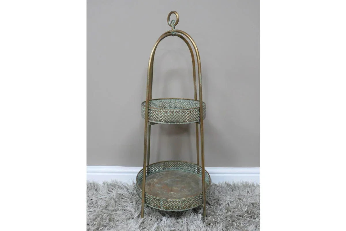 Two tier gold metal serving stand with patterned trays on a shaggy rug