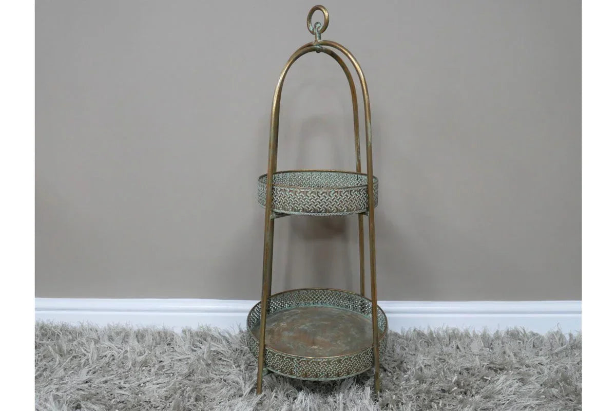 Two tier metal storage stand with ornate pattern, bronze finish, on grey rug