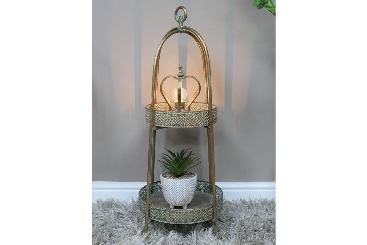 Two tier gold metal side table with decorative lamp and potted plant on textured grey rug