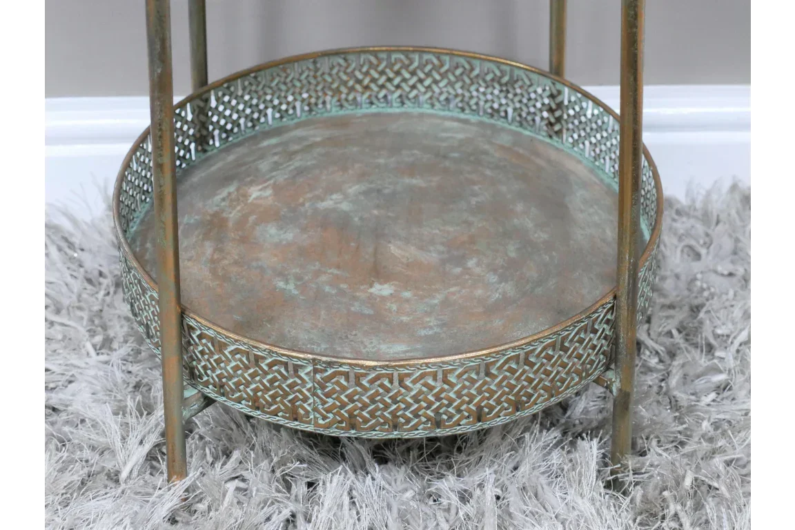 Round metal side table with distressed finish and patterned edge detail on grey rug
