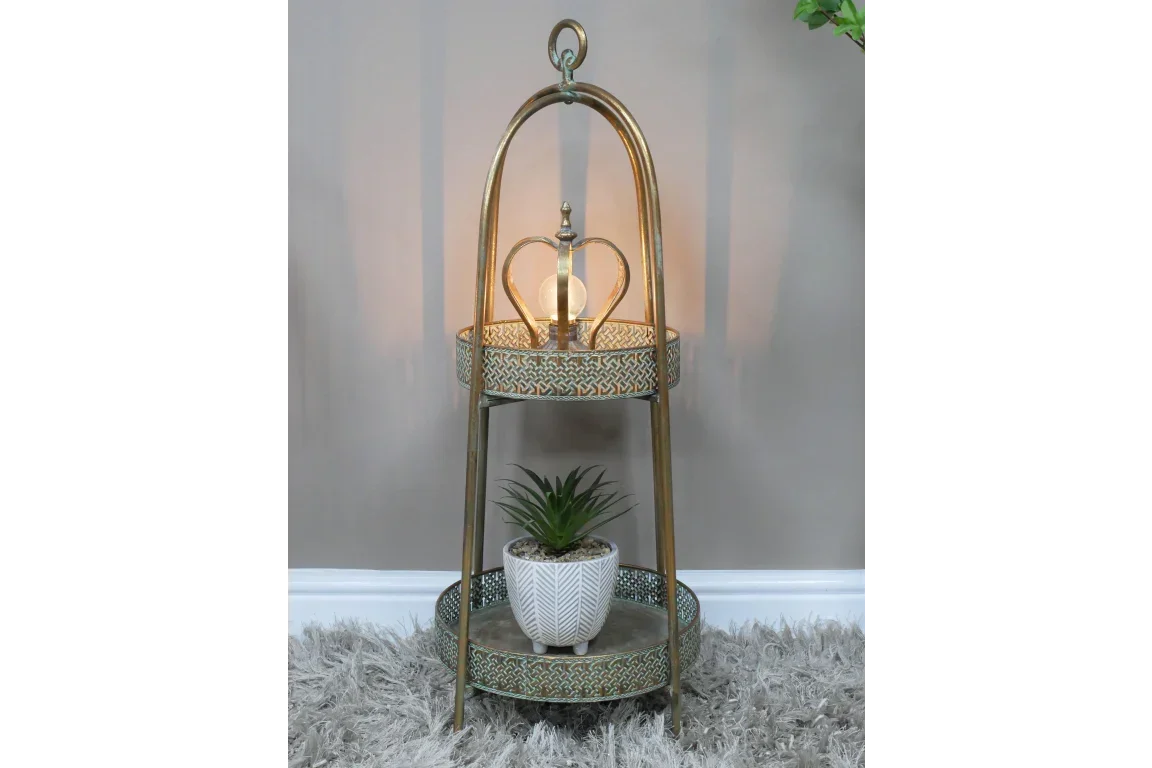 Gold metal side table with crown detail, lamp on top shelf, plant on lower shelf on carpet