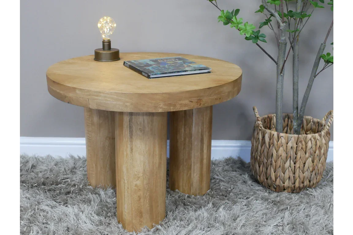 Round wooden coffee table with three pillar legs, lamp, and magazine on carpet