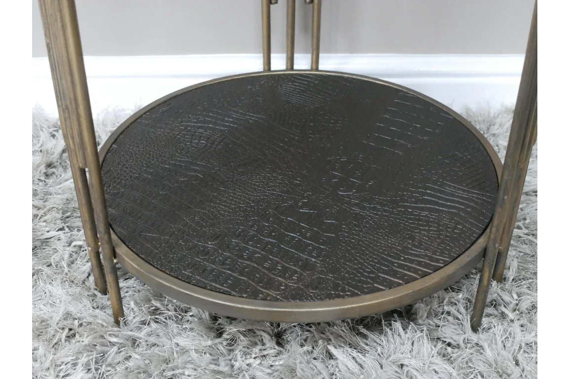 Round black metal side table with textured surface and gold legs on grey rug