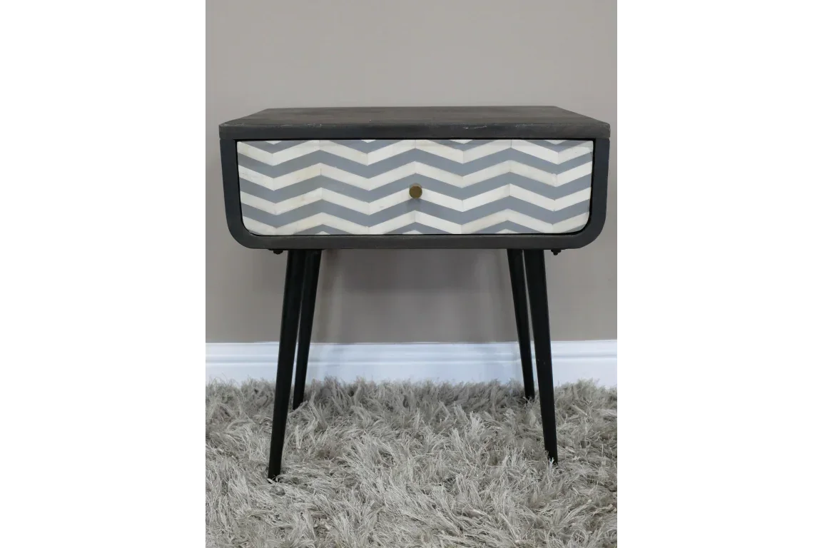 Modern bedside table with black legs and chevron pattern drawer front on grey rug