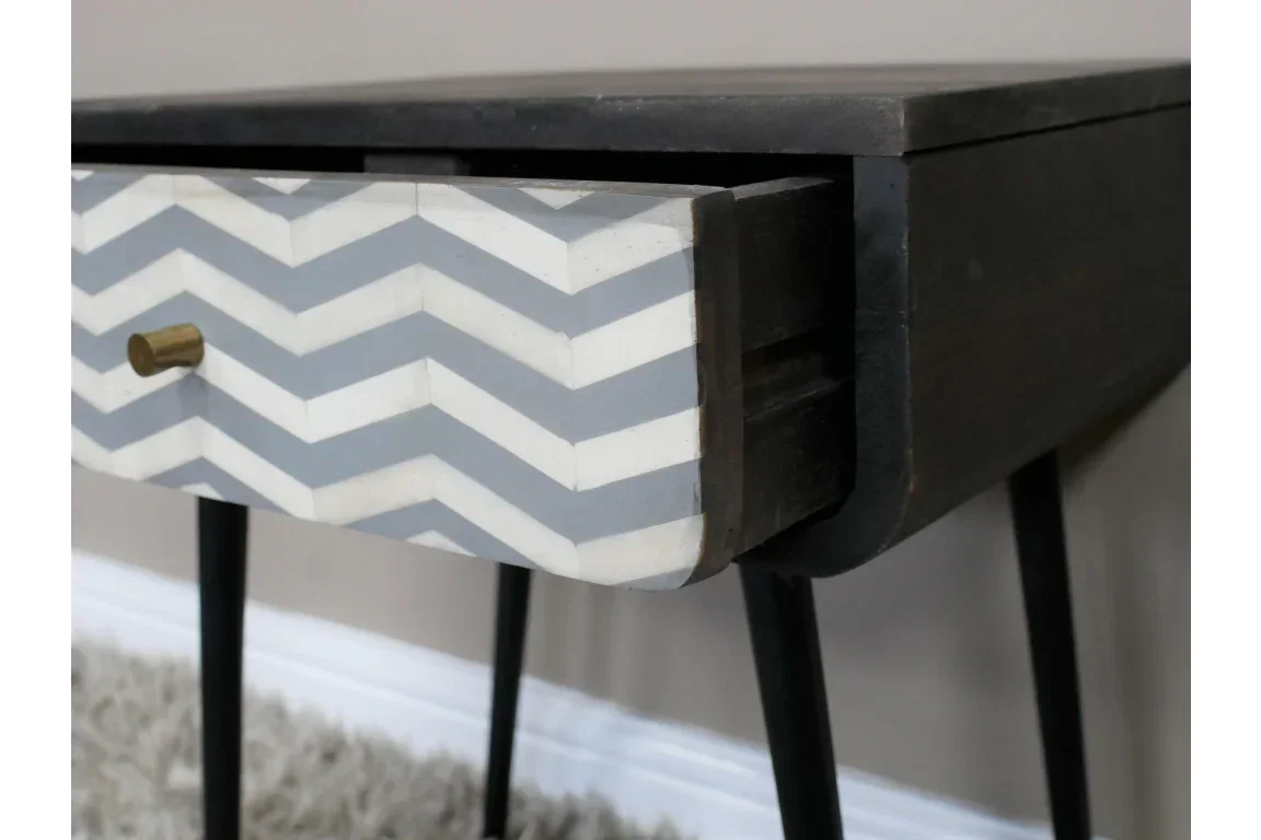 Wooden side table with chevron patterned drawer and brass handle on black legs