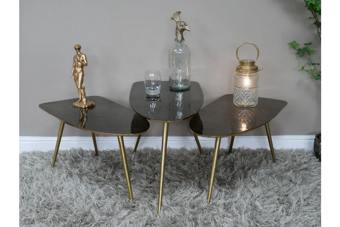 Set of three black glass coffee tables with gold legs on grey rug, decorated with ornaments