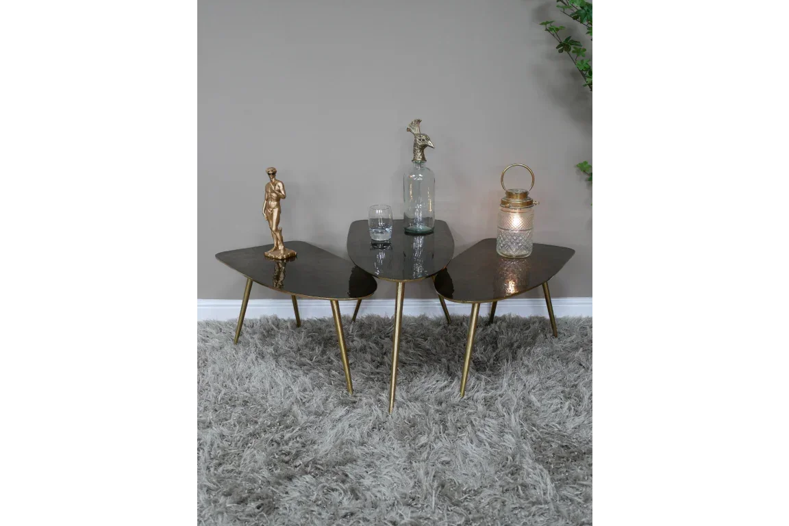 Set of three black glass coffee tables with gold legs on grey rug, decorative items on top