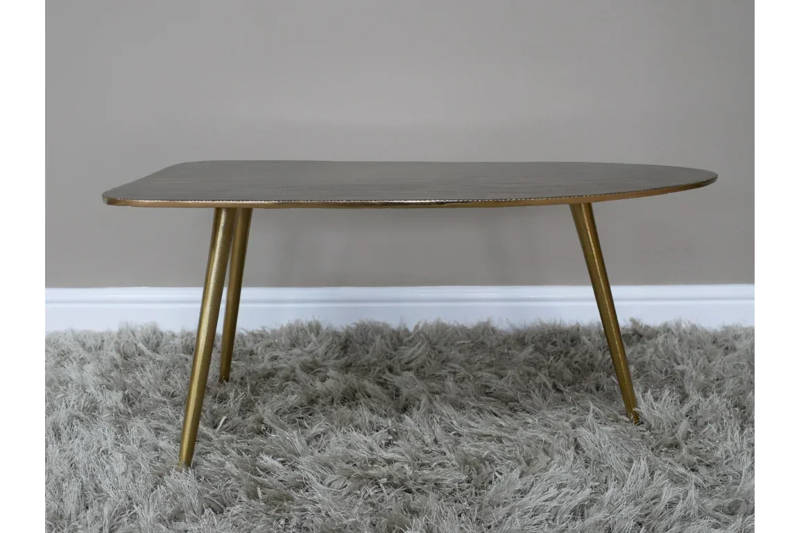 Gold metal coffee table with rounded edges on a grey shaggy rug against beige wall