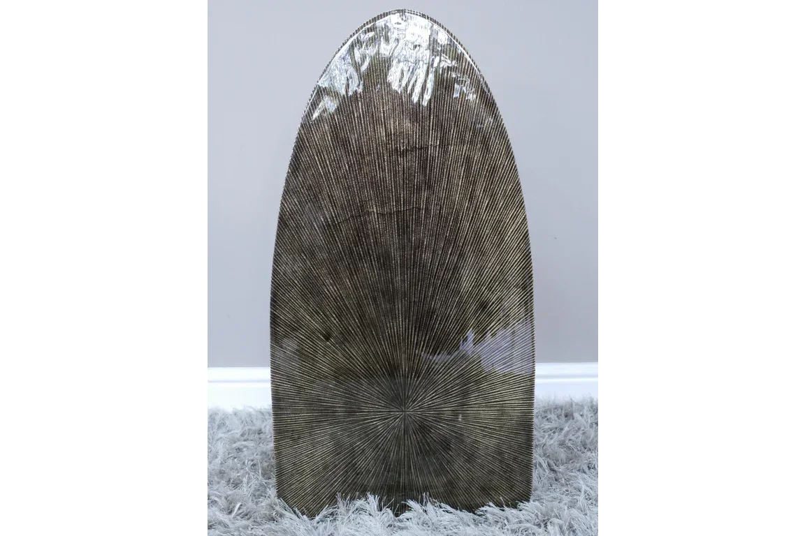 Metallic decorative vase with textured radial lines, standing on grey shaggy rug
