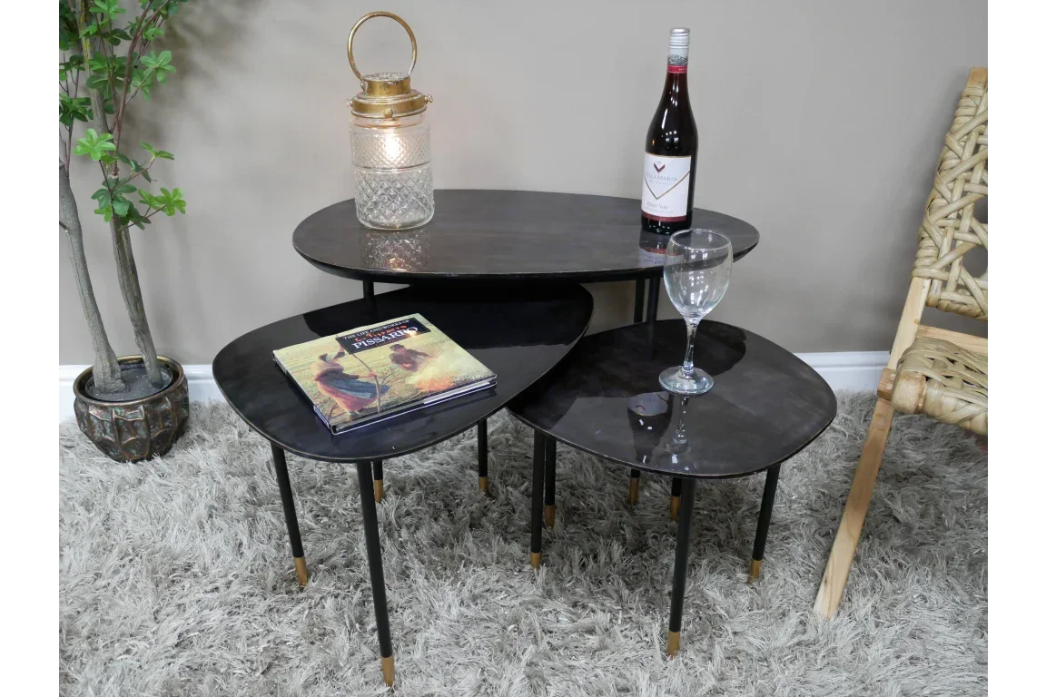 Set of three black nesting coffee tables with gold-tipped legs on a grey rug