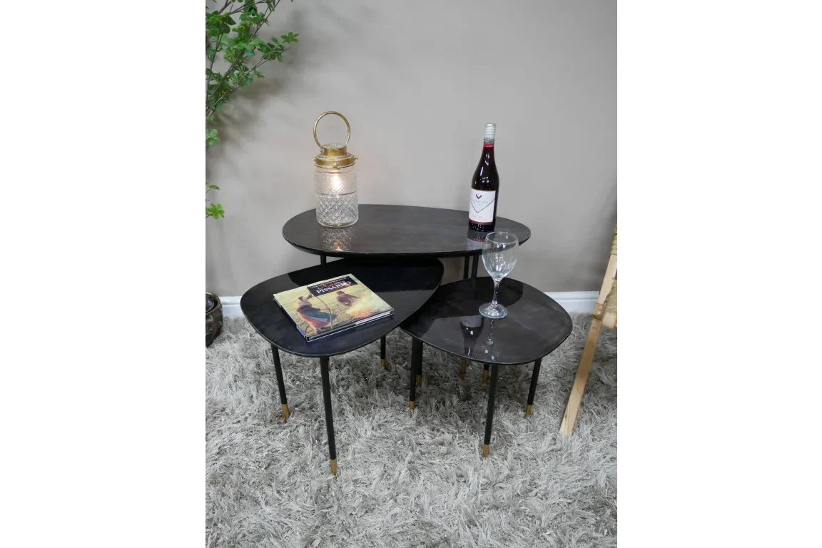 Black nesting coffee tables with gold feet, wine bottle, glass, candle and magazine on top
