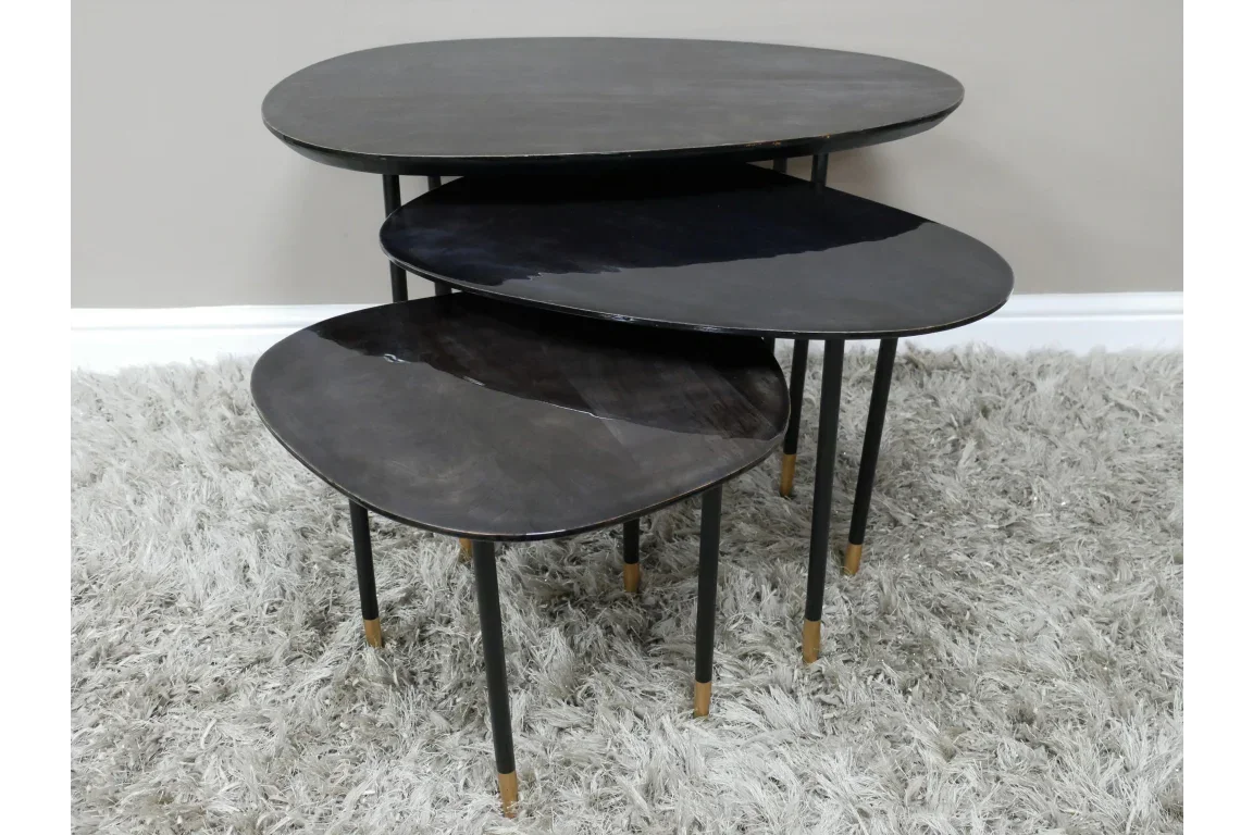 Set of three black nesting tables with gold-tipped legs on grey shaggy rug