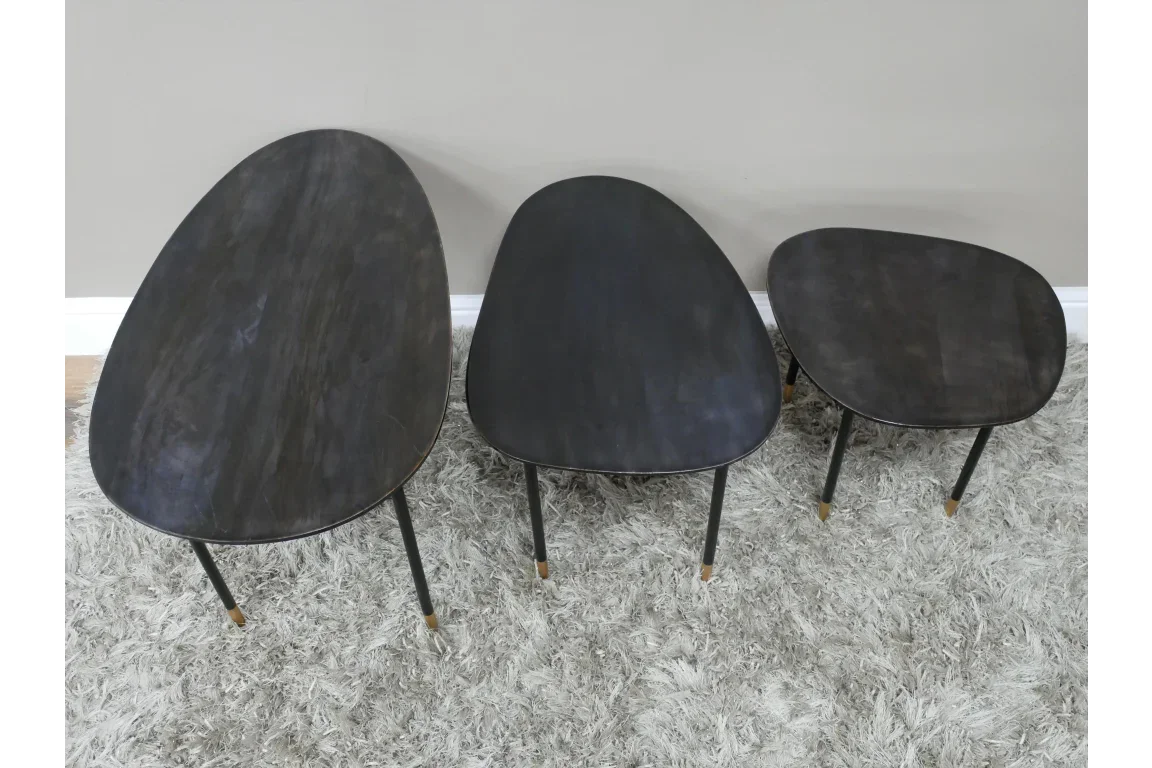 Set of three black wooden nesting coffee tables with gold-tipped legs on grey rug
