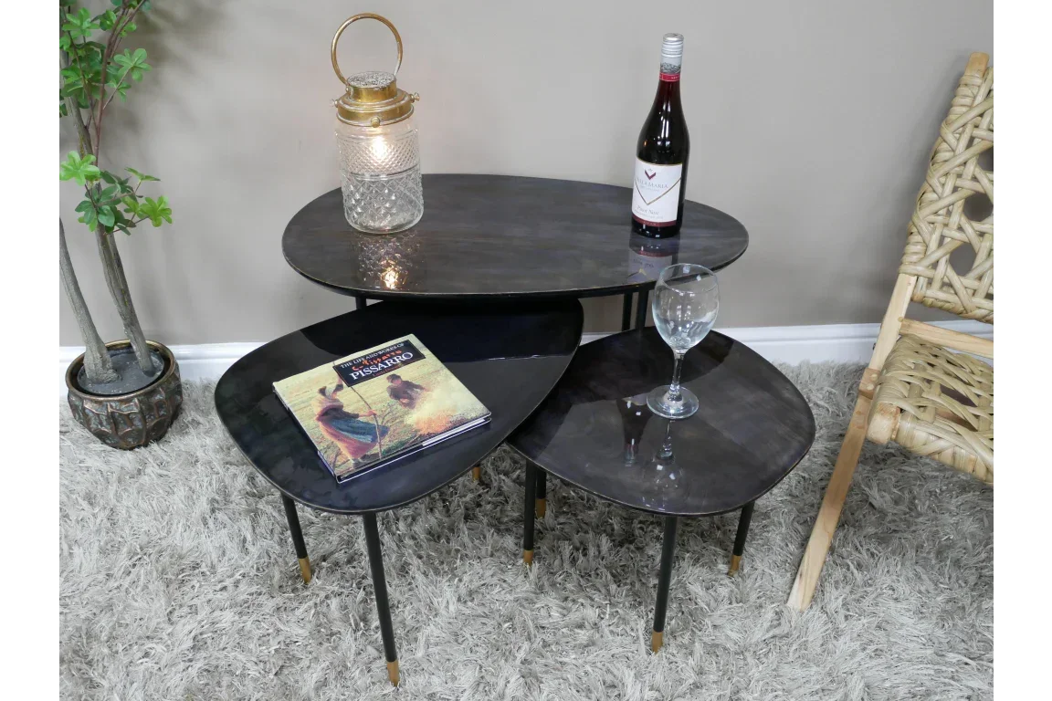 Set of three black nesting coffee tables with metal legs shown in living room setting