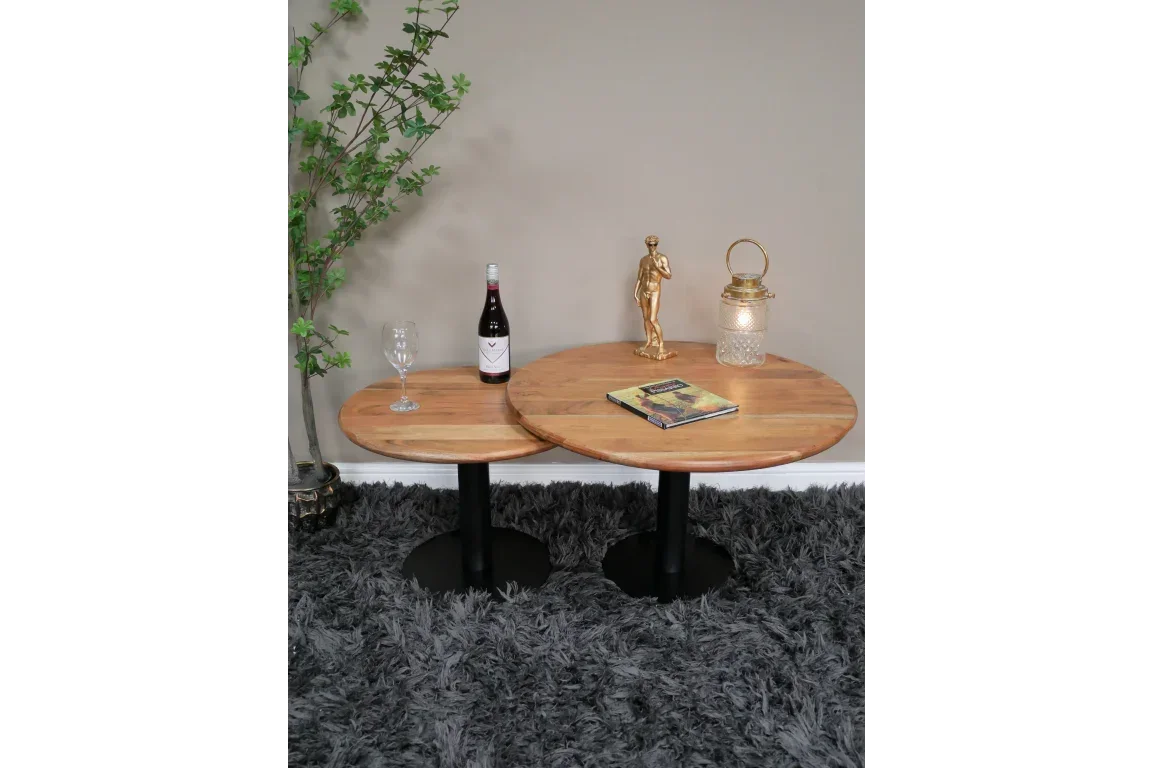 Set of two round wooden coffee tables with black bases on grey rug, decor and wine bottle