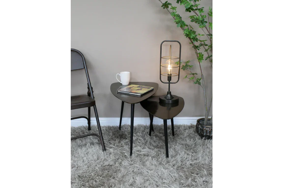 black nest of tables with lamp, mug and book on beige rug beside chair and indoor plant