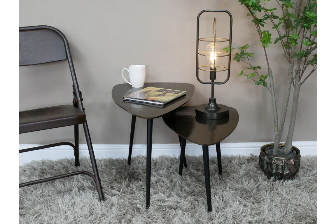 Set of two black nesting tables with lamp, book, and mug on grey rug next to chair