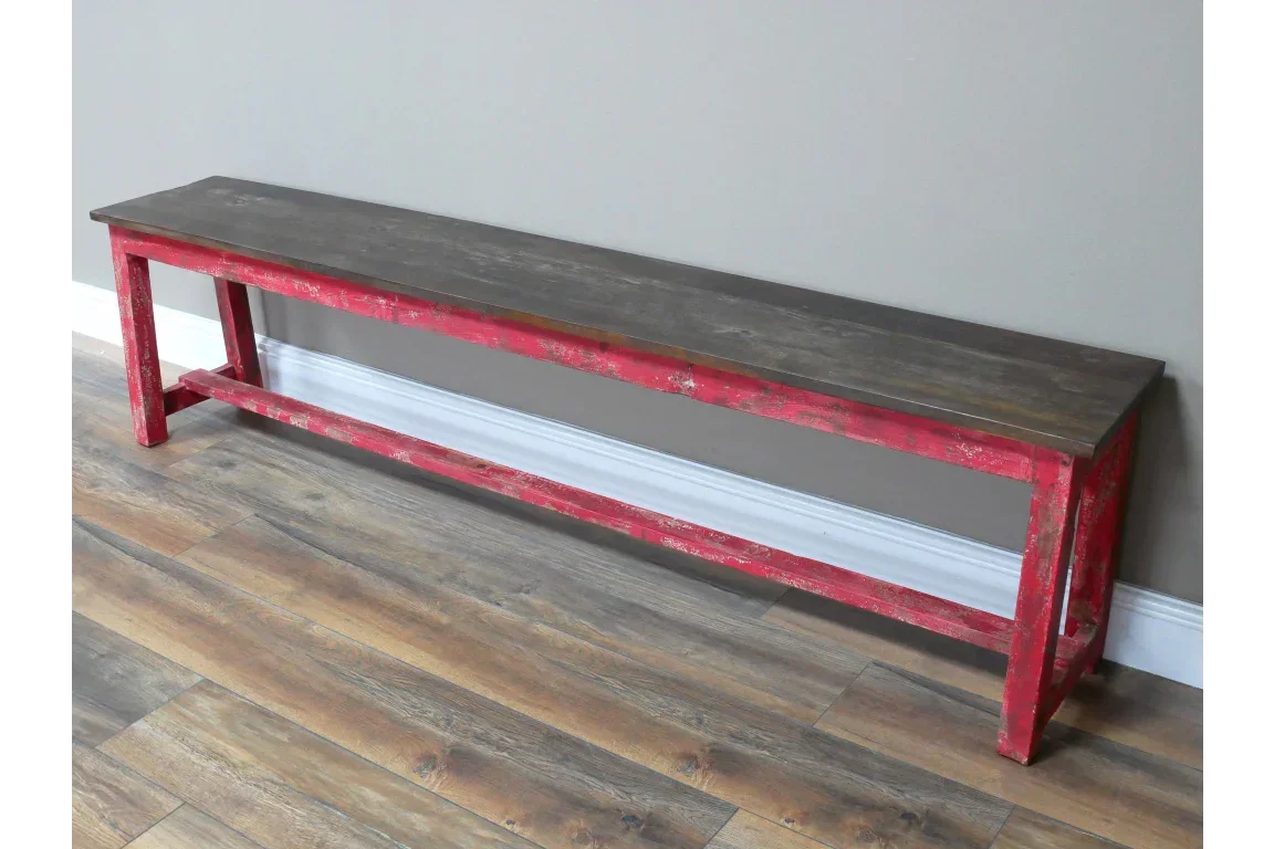 Wooden dining bench with distressed red frame and dark seat on laminate floor