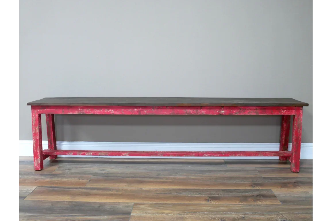 Distressed red wooden bench with dark top set against a neutral wall and wood floor