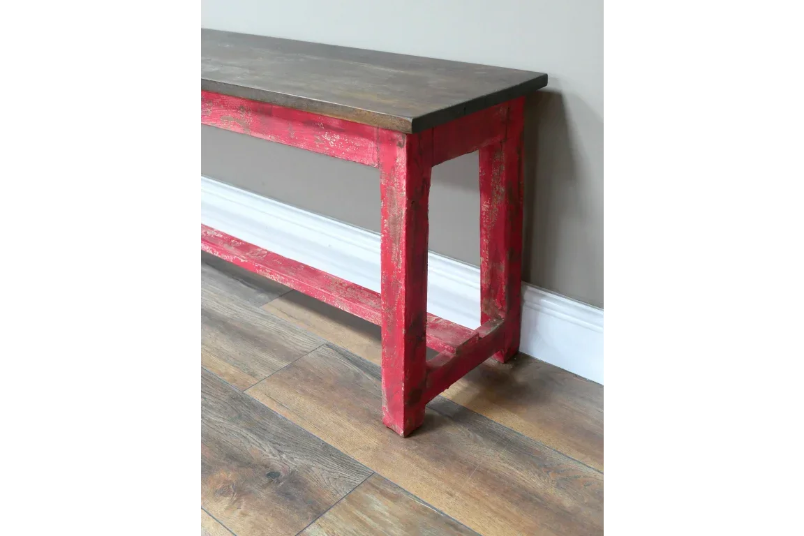 Rustic wooden bench with distressed red legs and dark wood seat on laminate floor