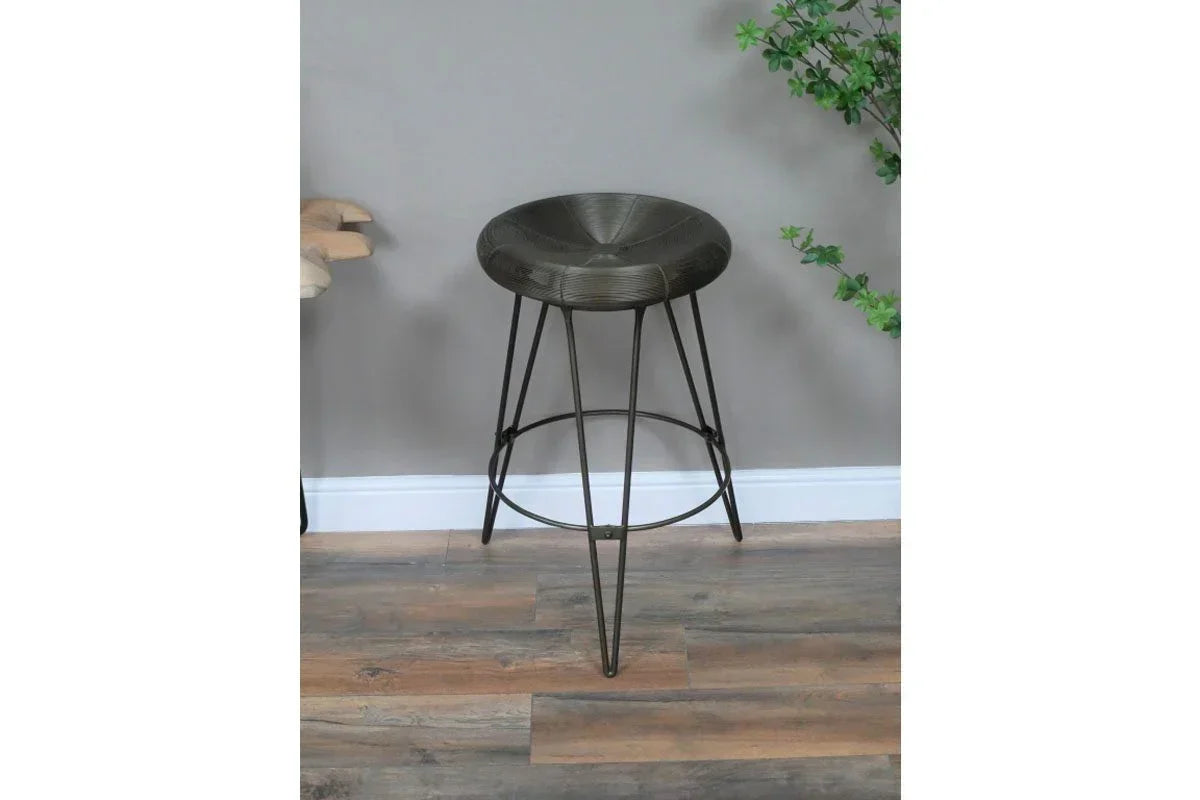 Metal bar stool with round seat and hairpin legs on wood floor against a grey wall