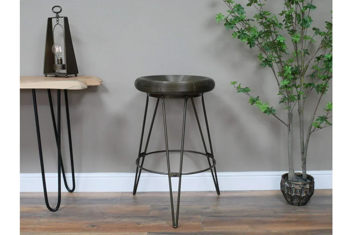 Industrial metal bar stool with round seat and hairpin legs beside console table and indoor plant