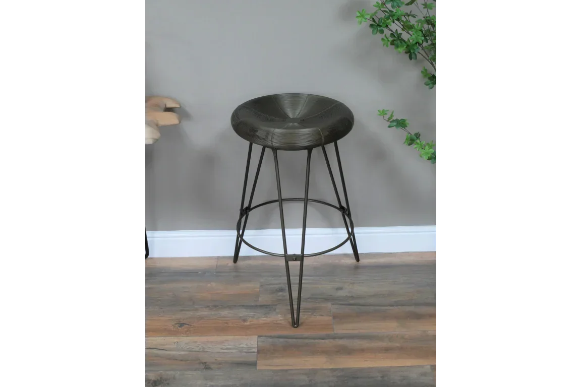 Metal bar stool with round seat and black hairpin legs on wood floor