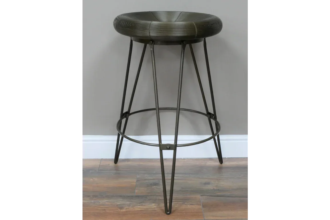 Metal bar stool with round textured seat and hairpin legs on wooden floor