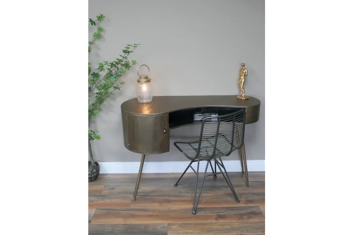 Brass-finish metal desk with storage, black wire chair, and decor on wooden floor