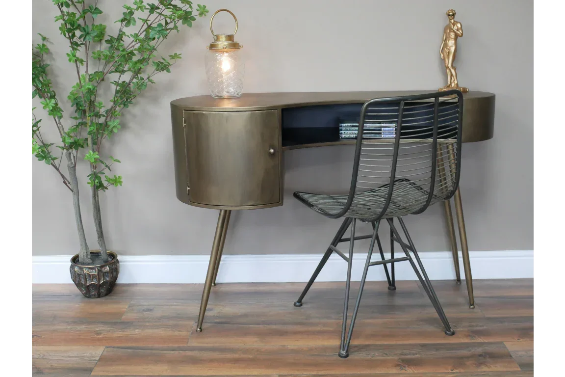 Brass metal desk with curved storage, wire chair, lamp and decor on wooden floor