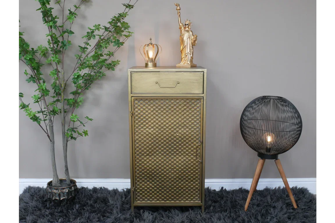 Gold cabinet with textured door, decorative lamp, and plant beside black tripod floor lamp